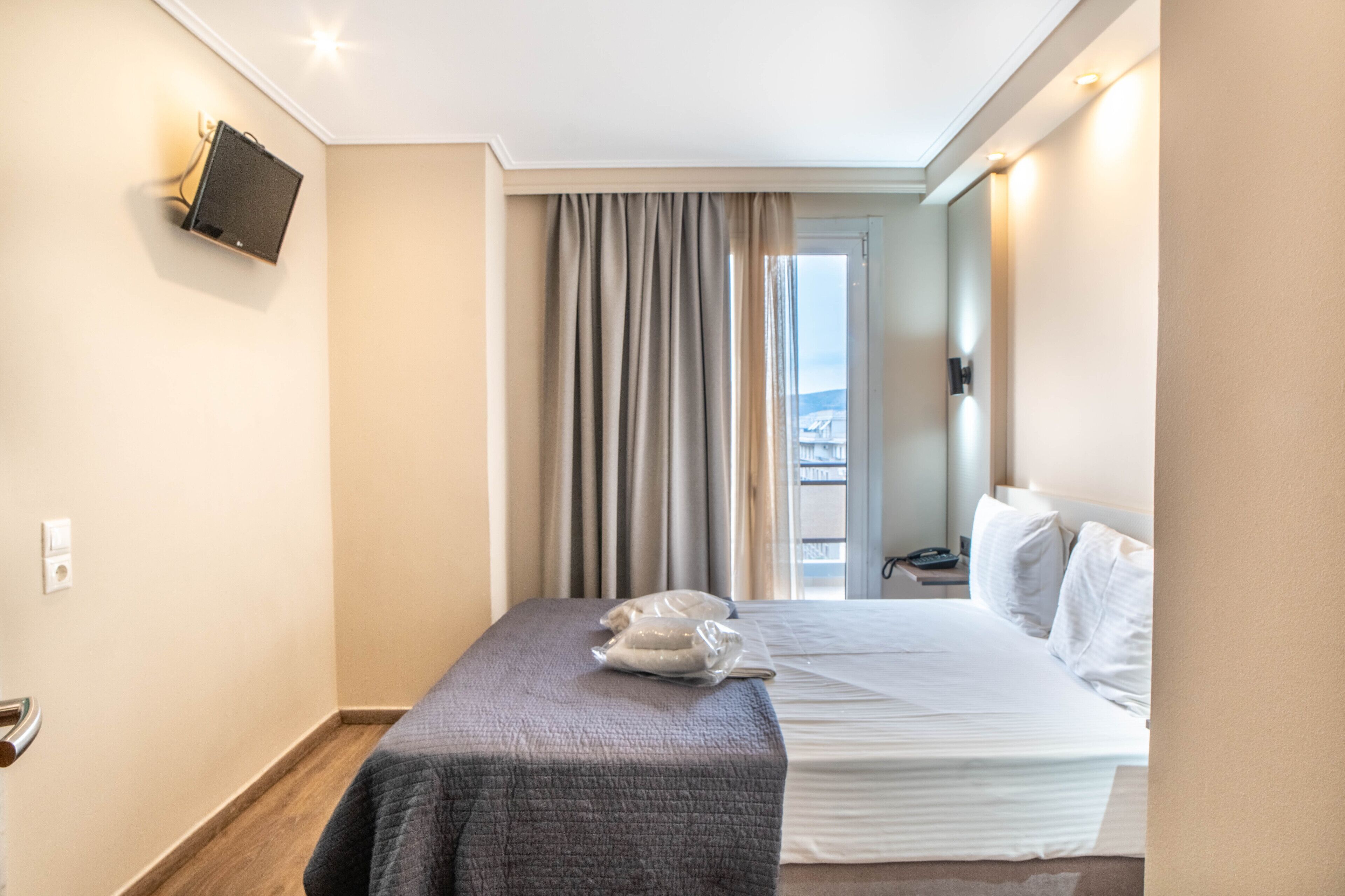 Een hotelkamer met een bed, een wandtelevisie, een raam met gordijnen en uitzicht op buiten.