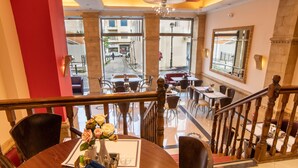 A hotel lobby with a dining area, a staircase, and a view of the street outside. - Argo Hotel (Piraeus)