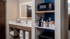 A modern bathroom with a white sink, a mirror, a microwave, a coffee maker, and a trash bin. - Holiday Inn Express Charleston-Kanawha City by IHG (Charleston)