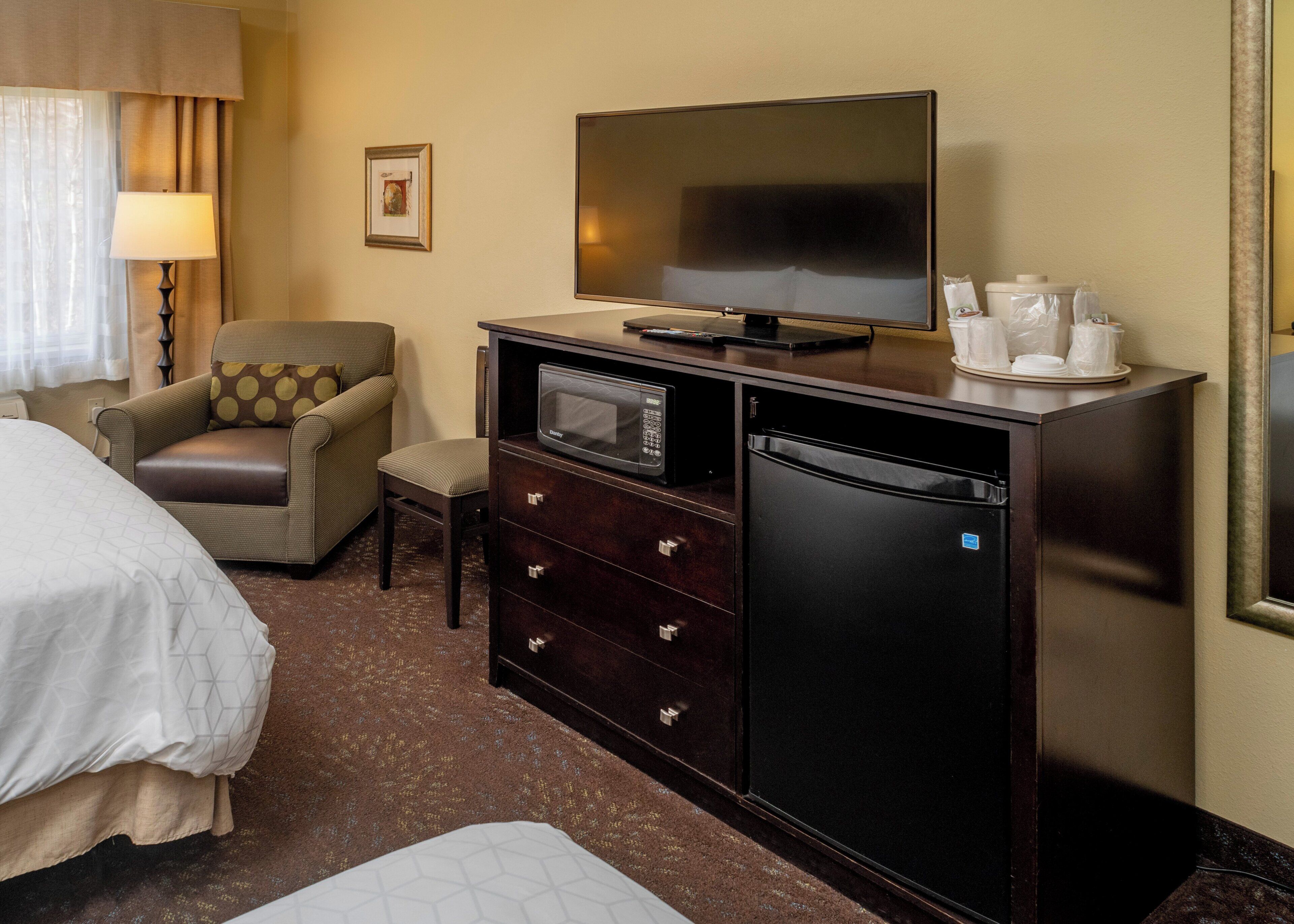 Una habitación de hotel con cama, sofá, escritorio con televisor, microondas, refrigerador y cafetera.