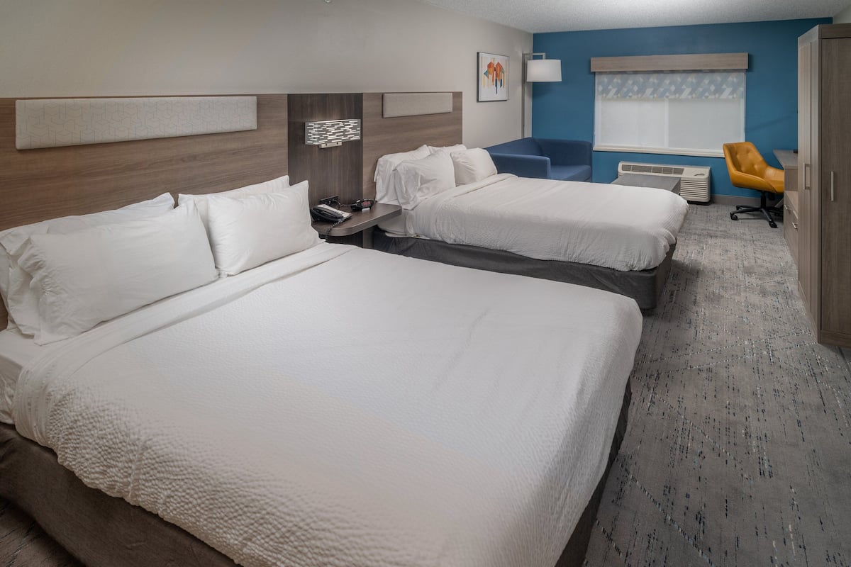 A hotel room with two beds, a desk, a chair, and a window with blinds.