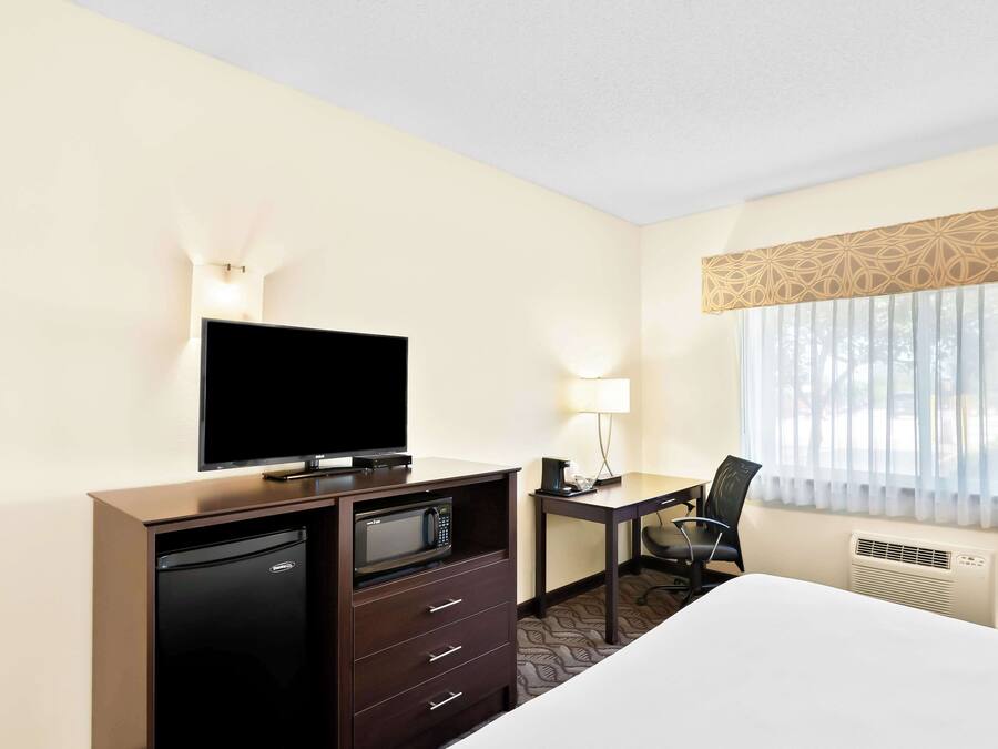 A hotel room with a bed, a desk with a chair, a television, a microwave, and a lamp.