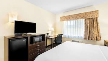 Een hotelkamer met een bed, een bureau met stoel, een televisie, een minibar en een lamp.