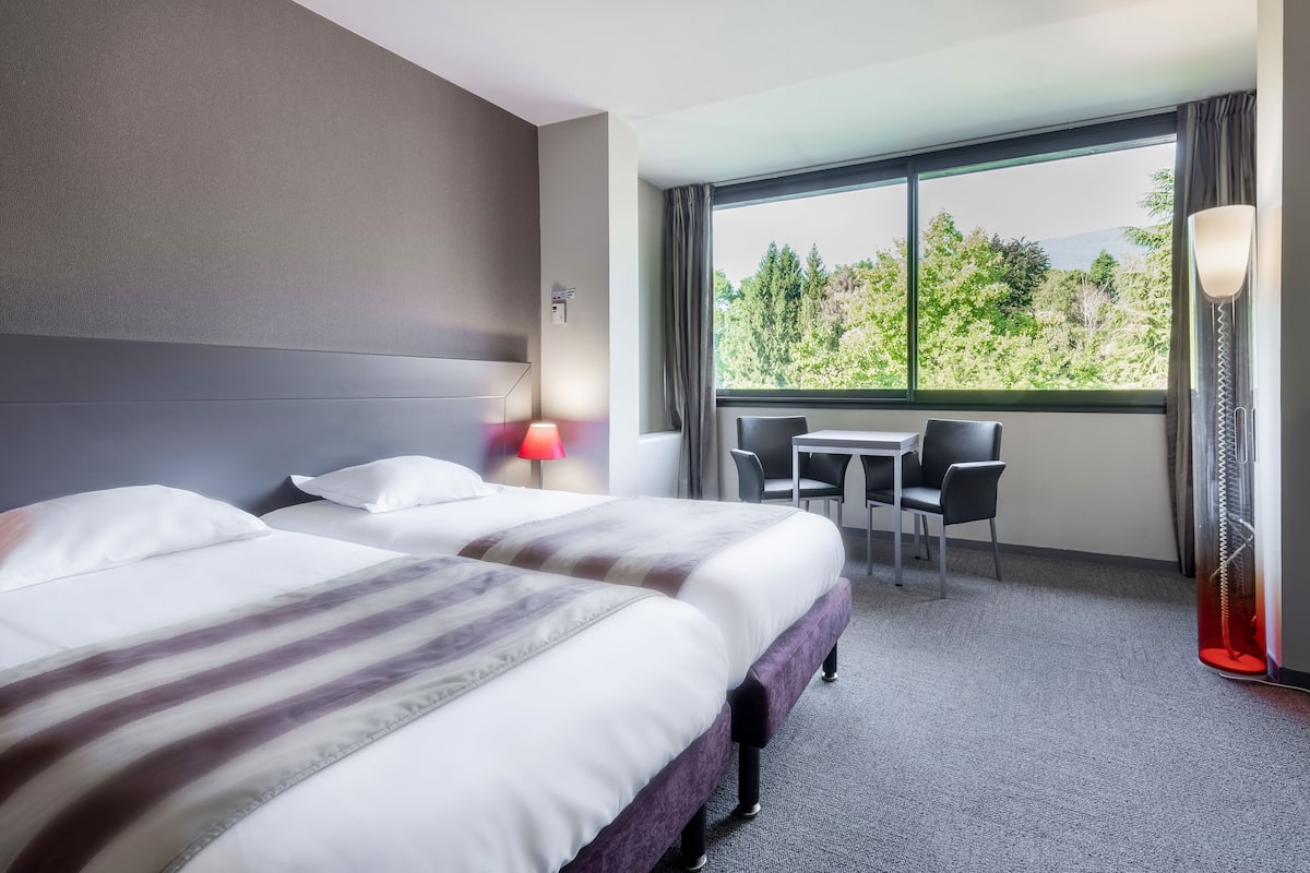Quarto de hotel com duas camas, uma escrivaninha e uma cadeira.