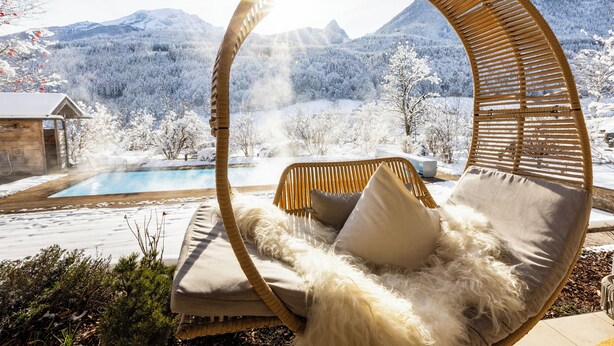 A wicker chair with a fluffy cushion in a snowy landscape with a pool and mountains in the background. - Berghotel Rehlegg (Ramsau bei Berchtesgaden)