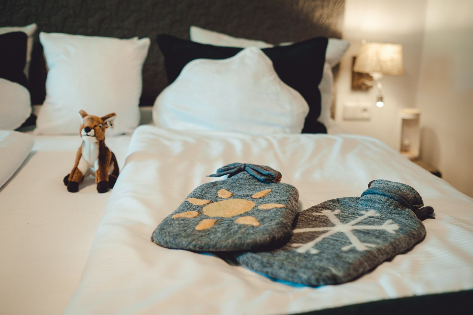 Una cama bien hecha con ropa blanca, un peluche pequeño y dos almohadas decorativas con estampados de animales.