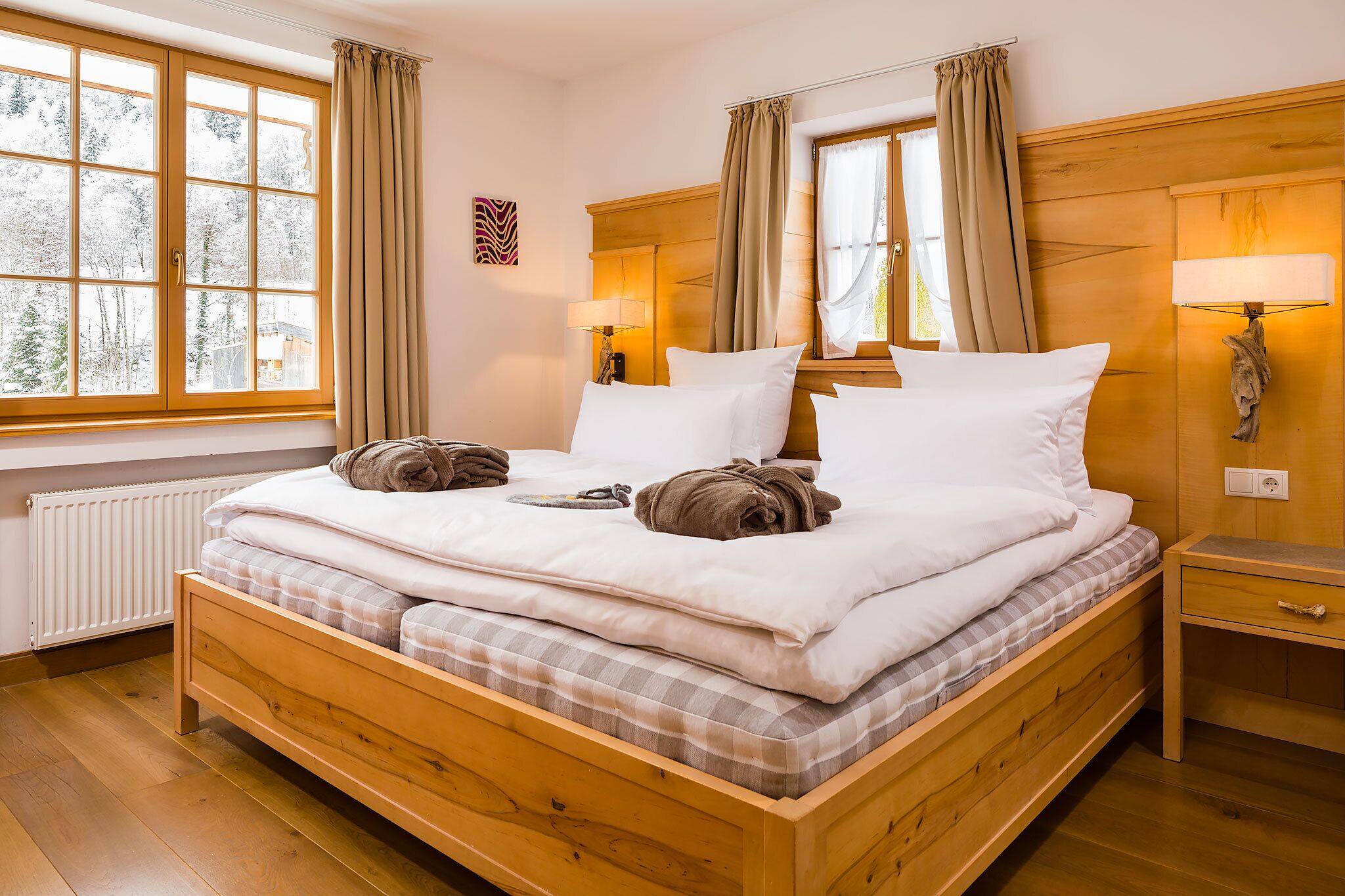 Una cama de madera con ropa de cama blanca, una mesita de noche con lámpara y una ventana con cortinas.