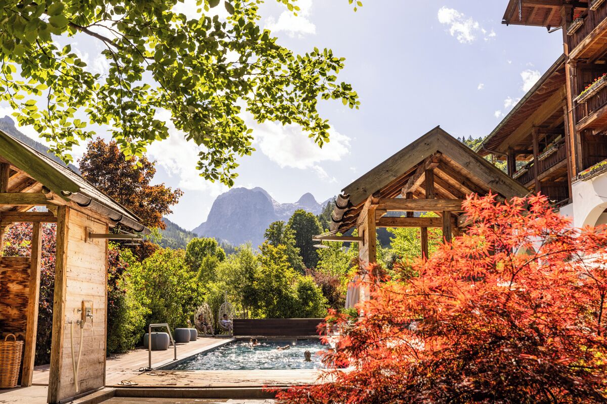 A wooden spa area with a hot tub, surrounded by lush greenery and a mountain backdrop.