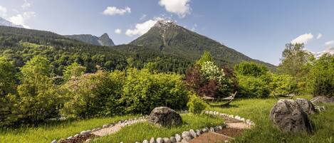 Un paisaje montañoso con cielo despejado, un jardín con un sendero de piedra y un banco de madera.