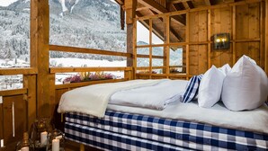 A wooden cabin with a bed, a window with a view of snow-covered mountains, and a candle on the windowsill. - Berghotel Rehlegg (Ramsau bei Berchtesgaden)