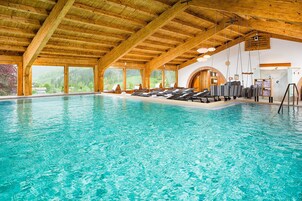 Una piscina interior con vigas de madera, tumbonas y ventanas amplias que ofrecen vistas al exterior.