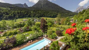 Ein Pool mit Holzterrasse, umgeben von Grünpflanzen und roten Blüten.