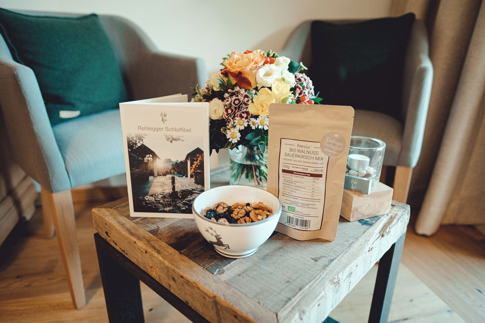 Una mesa de madera con un cuenco de nueces, un ramo de flores, una tarjeta y un paquete de mezcla orgánica de cerezas agrias y nueces.