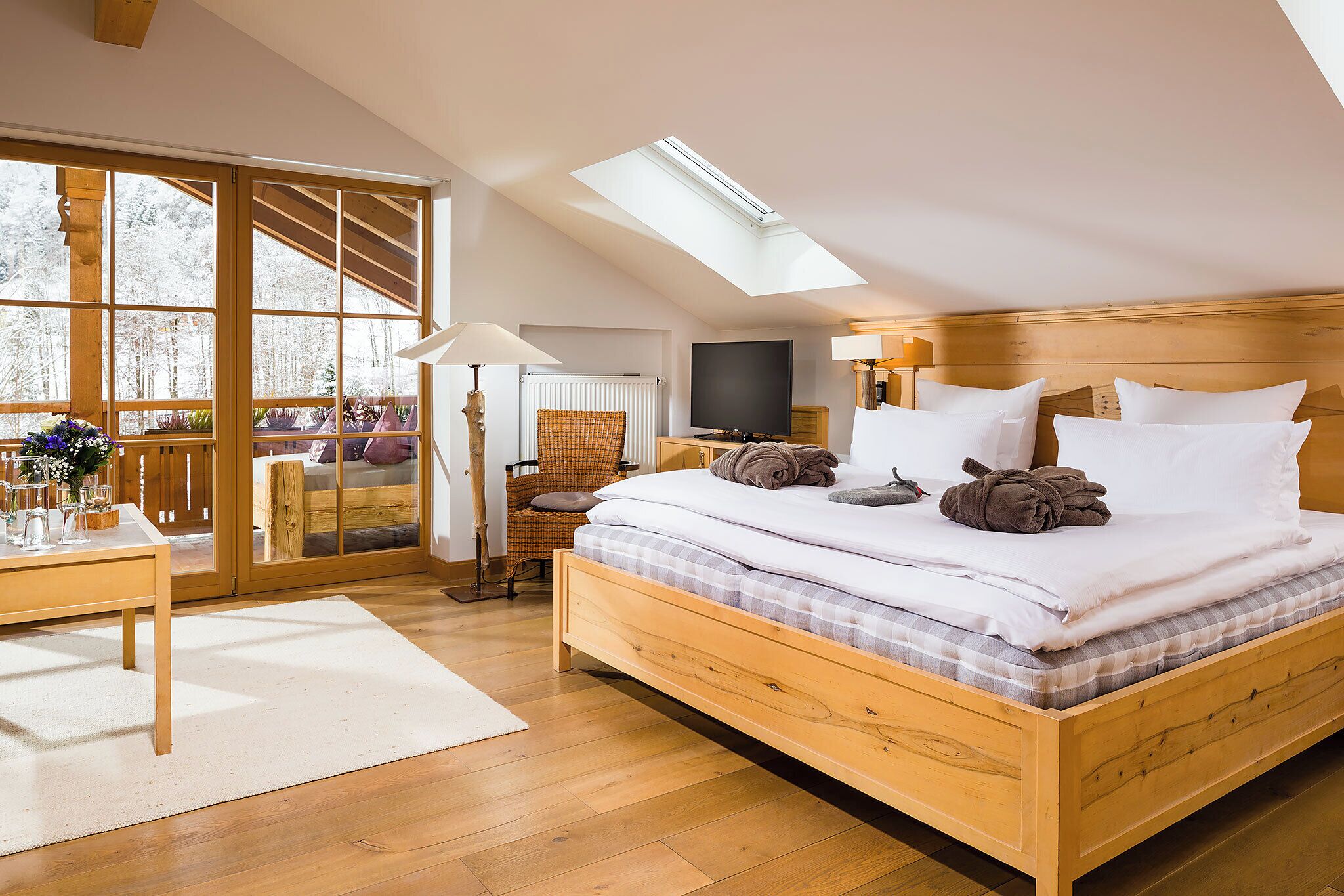 Ein Schlafzimmer mit Dachfenster, einem Bett mit Kissen, einem Fernseher und Blick ins Freie.