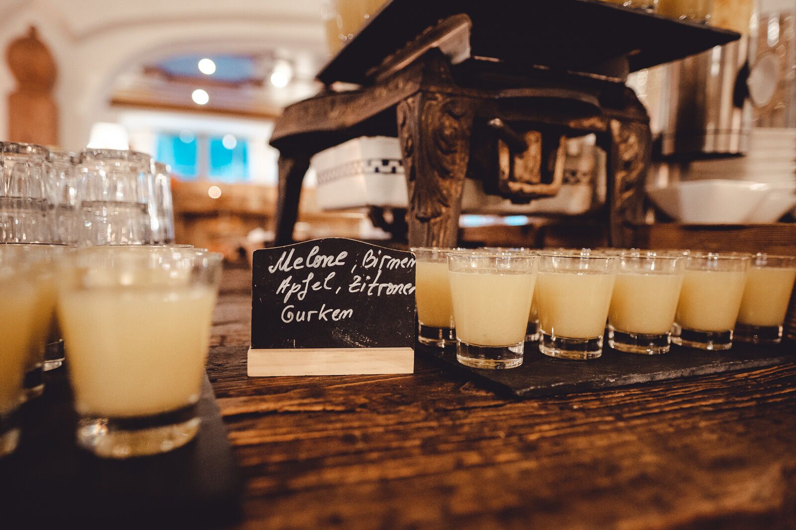 A bar area with shot glasses of beverages and a chalkboard menu listing items like Melone, Birmem, Apfel, Zitronc, and Gurkem.