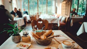 A dining table with bread, a cup of coffee, and a small plant.