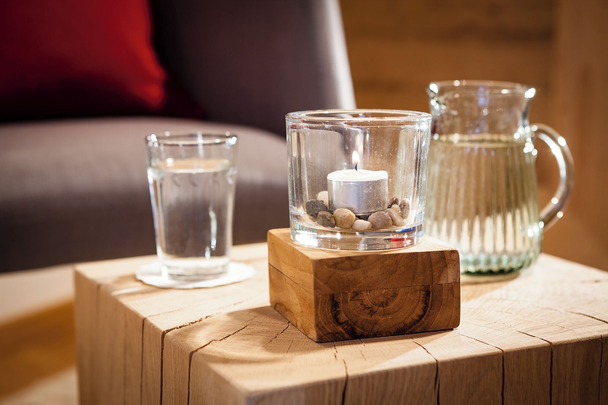 A wooden table with a glass candle holder and a glass pitcher on it.
