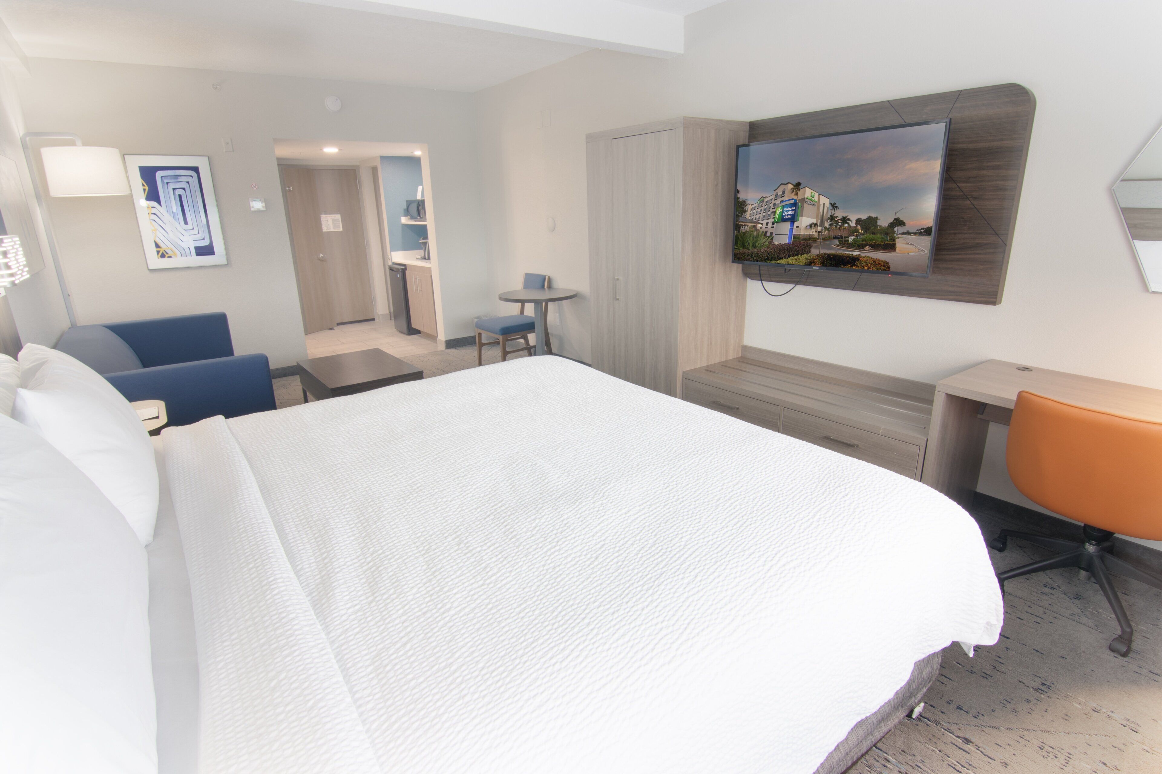 A hotel room with a large bed, a desk, a chair, a TV mounted on the wall, and a small table with a chair.
