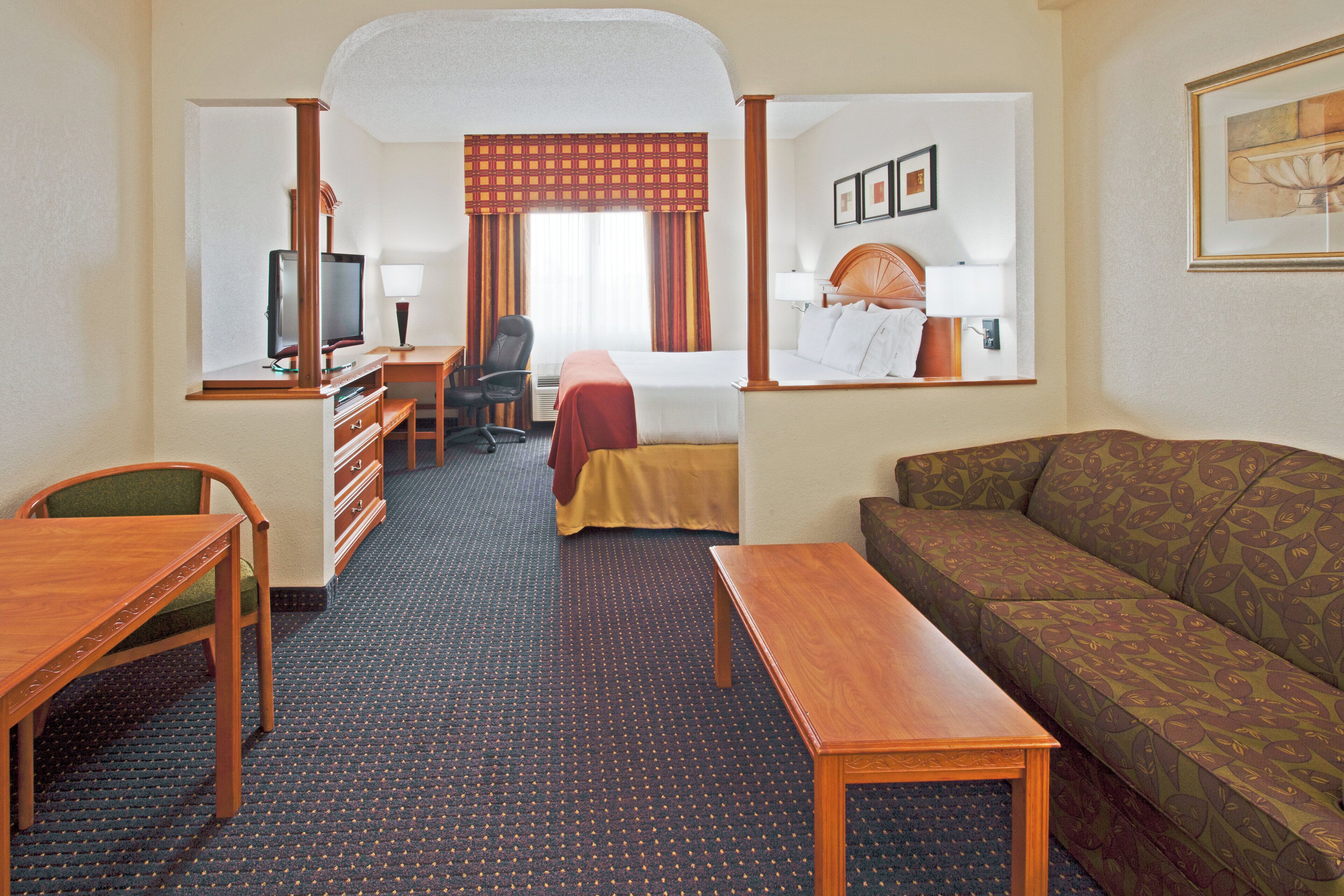 Une chambre d’hôtel comprenant un lit, un canapé, un bureau, une télévision et un miroir.