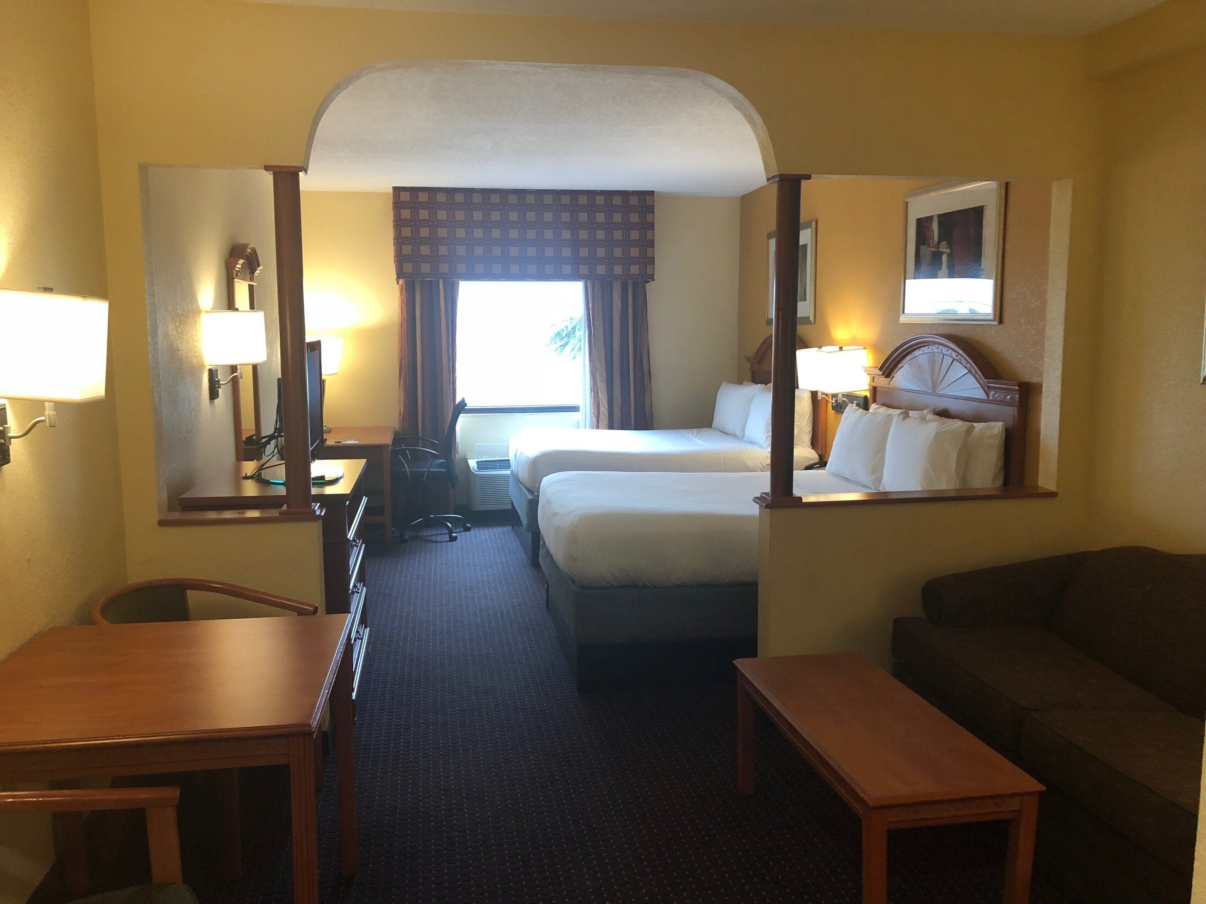 A hotel room with two beds, a desk, a chair, a sofa, and a mirror.