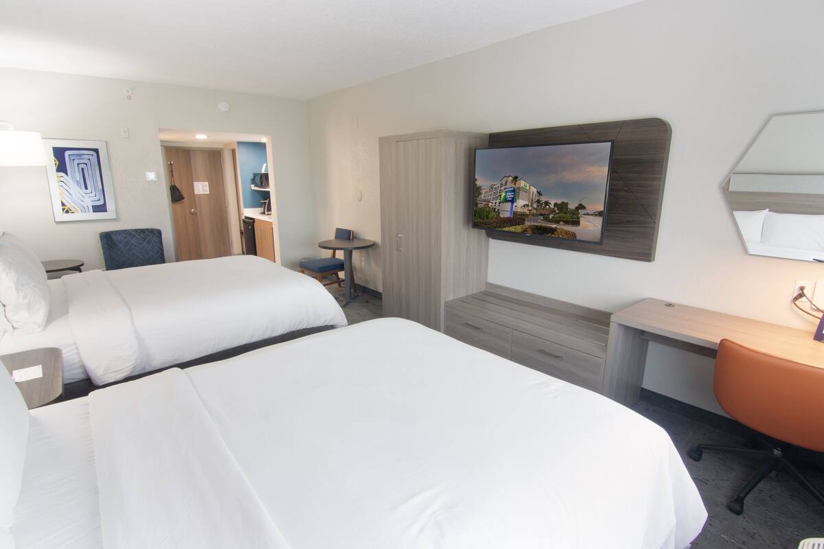 A hotel room with two beds, a desk, a chair, a TV, and a painting on the wall.
