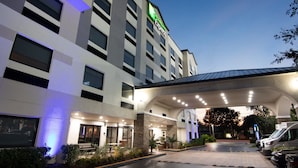 Ein Hotel mit modernem Design, mit einer auffälligen grün-weißen Schilderung, einer überdachten Eingangspforte und einem Parkplatz mit mehreren Fahrzeugen.