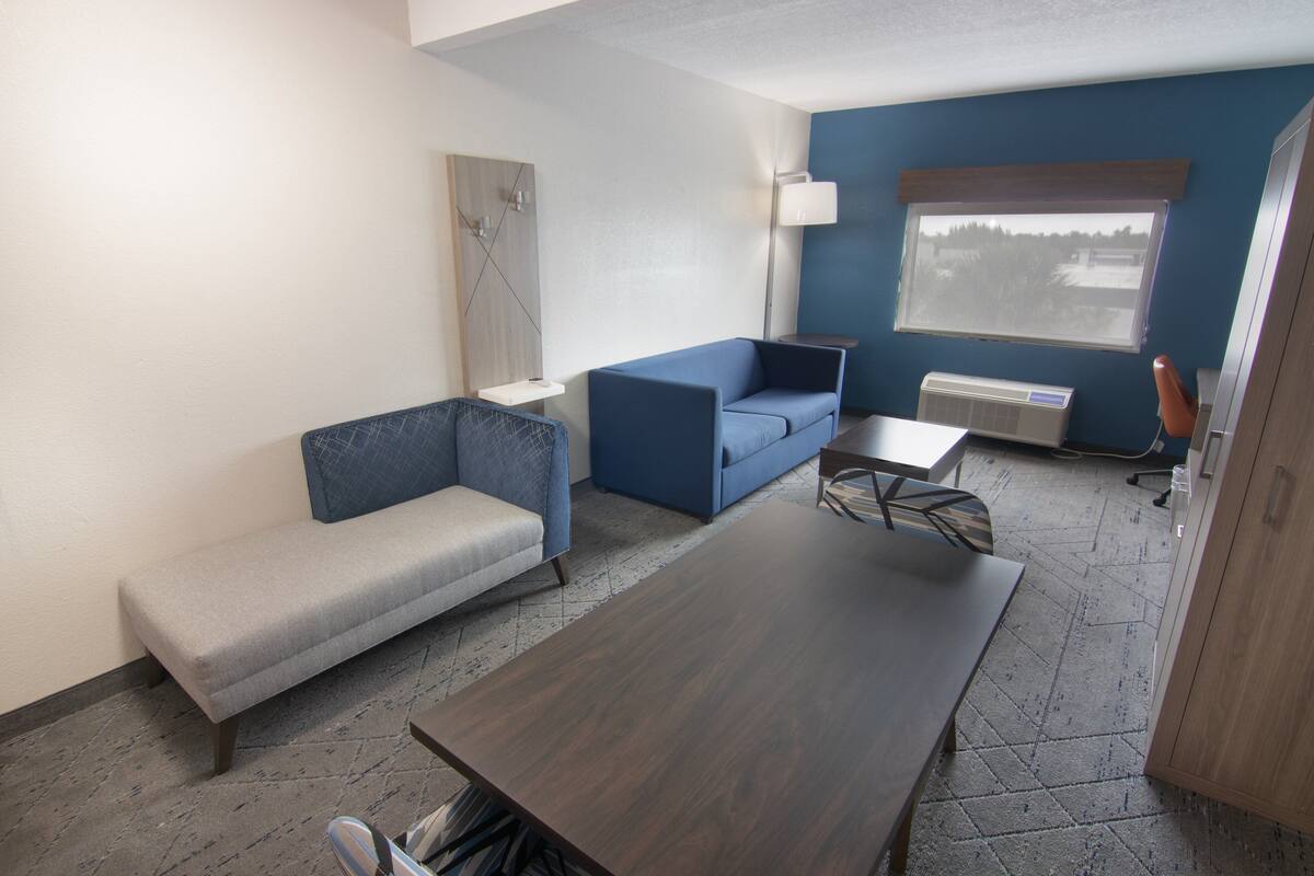A modern room with a grey sofa, a blue armchair, a wooden table, and a window with a view of trees.