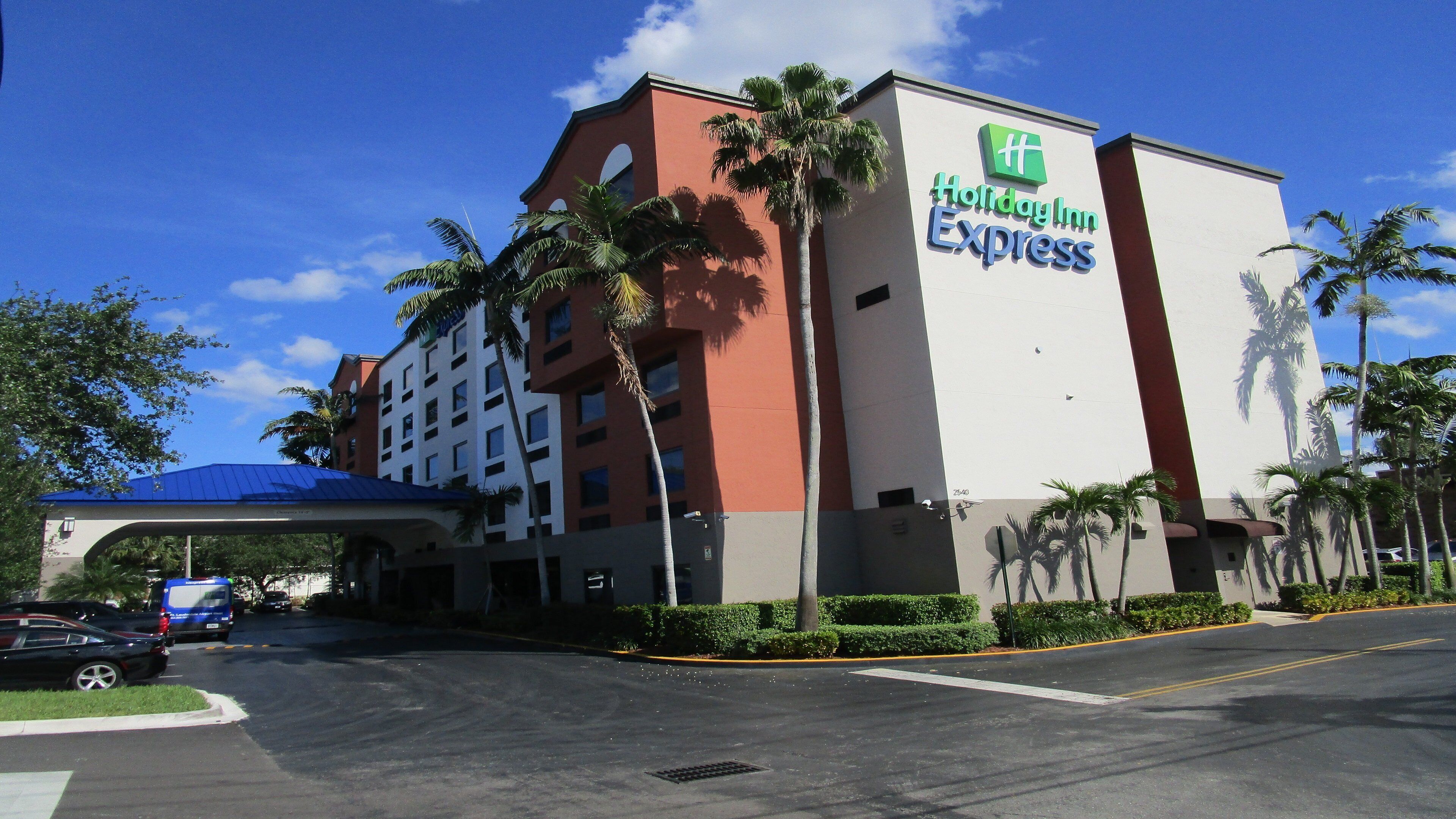 A Holiday Inn Express building with a flat roof, palm trees, and a clear sky.