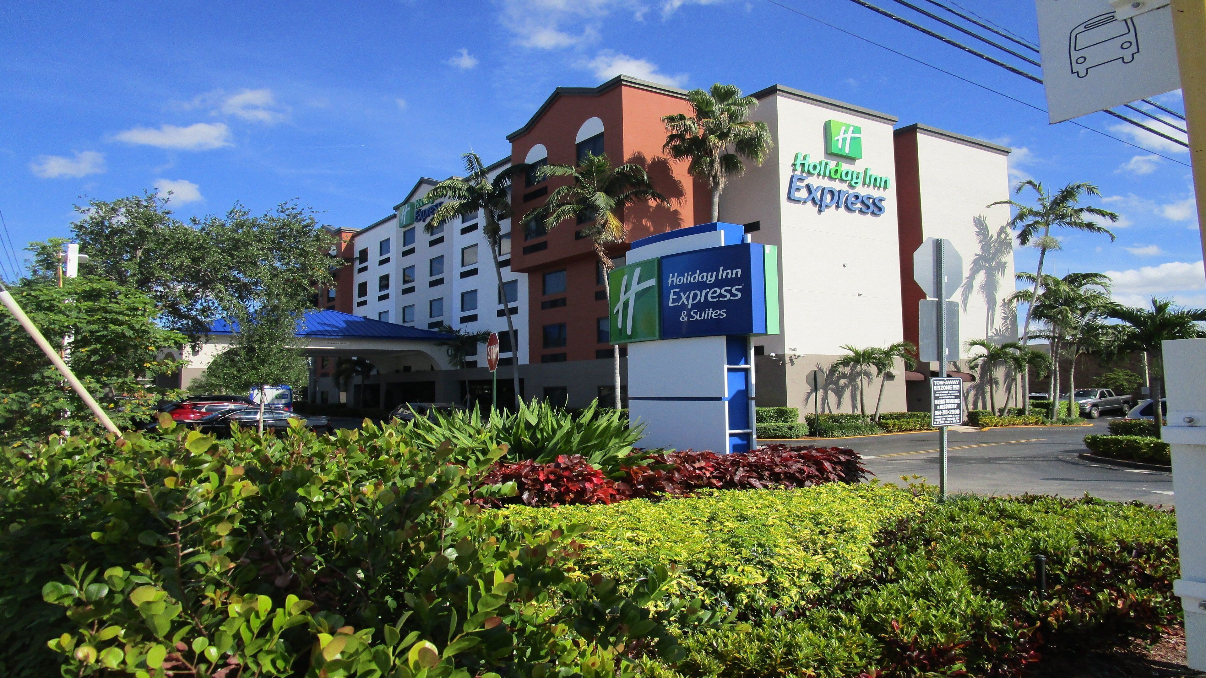 A Holiday Inn Express & Suites building with a clear sky, palm trees, and a parking lot.