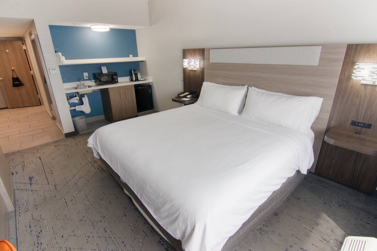 A hotel room with a large bed, a small kitchenette, and a separate bathroom area.