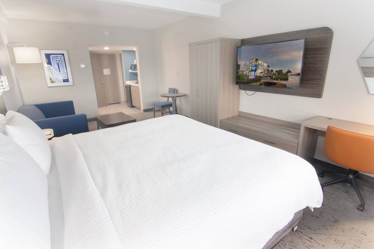 A hotel room with a large bed, a desk, a chair, a TV mounted on the wall, and a small table with a chair.