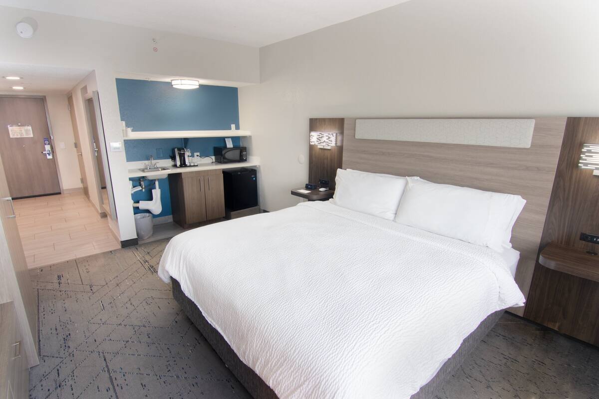 A hotel room with a large bed, a desk with a computer, a microwave, and a small kitchenette.