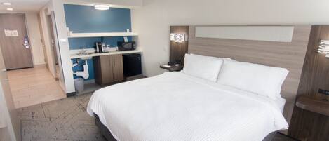 A hotel room with a large bed, a kitchenette, a bathroom, and a door leading to another room.
