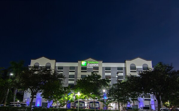 A Holiday Inn Express building at night with a sign, parking lot, and trees in front. - Holiday Inn Express & Suites Ft. Lauderdale Airport West by IHG (Davie)