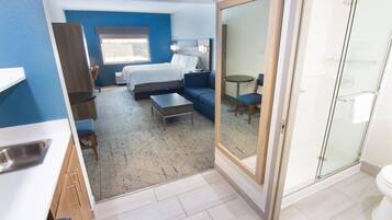 Habitación de hotel con cama, sofá, mesita, silla, baño con inodoro y zona de ducha.