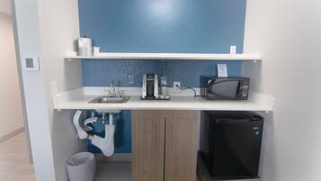 A compact kitchenette with a microwave, coffee maker, and sink.