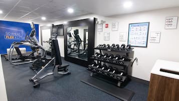 A gym with exercise equipment, a mirror, and a wall with instructional posters.