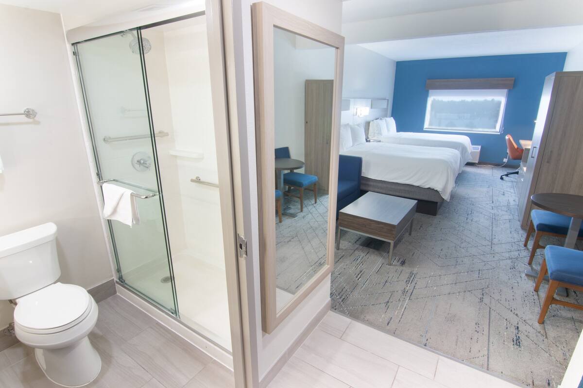 A hotel room with a glass shower enclosure, a bed, a desk, and a chair.