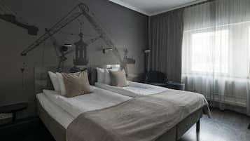 Habitación de hotel con dos camas, un ventanal con cortinas translúcidas, un mural de una grúa y una mesita de noche.