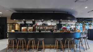 Un área de bar moderna con una barra curva, varios taburetes y una amplia variedad de botellas y vasos.