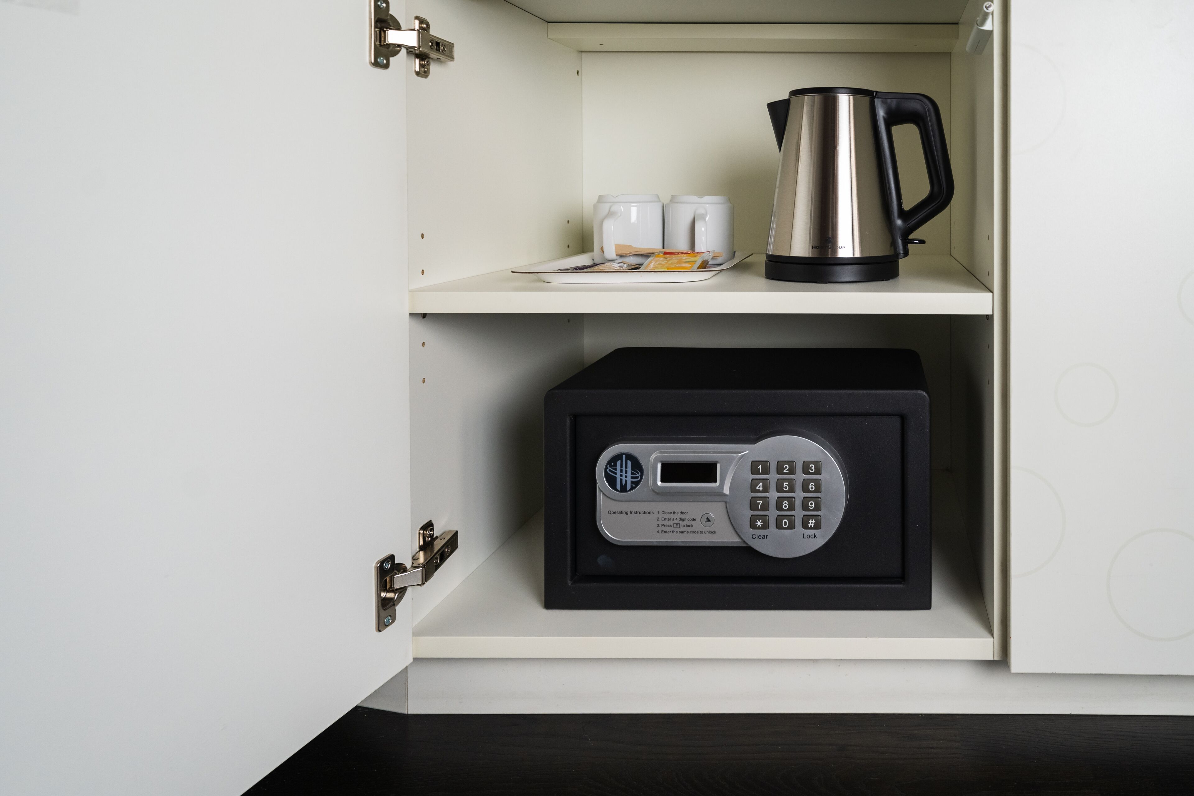 Un meuble de cuisine contenant une machine à café, deux tasses et un coffre-fort.