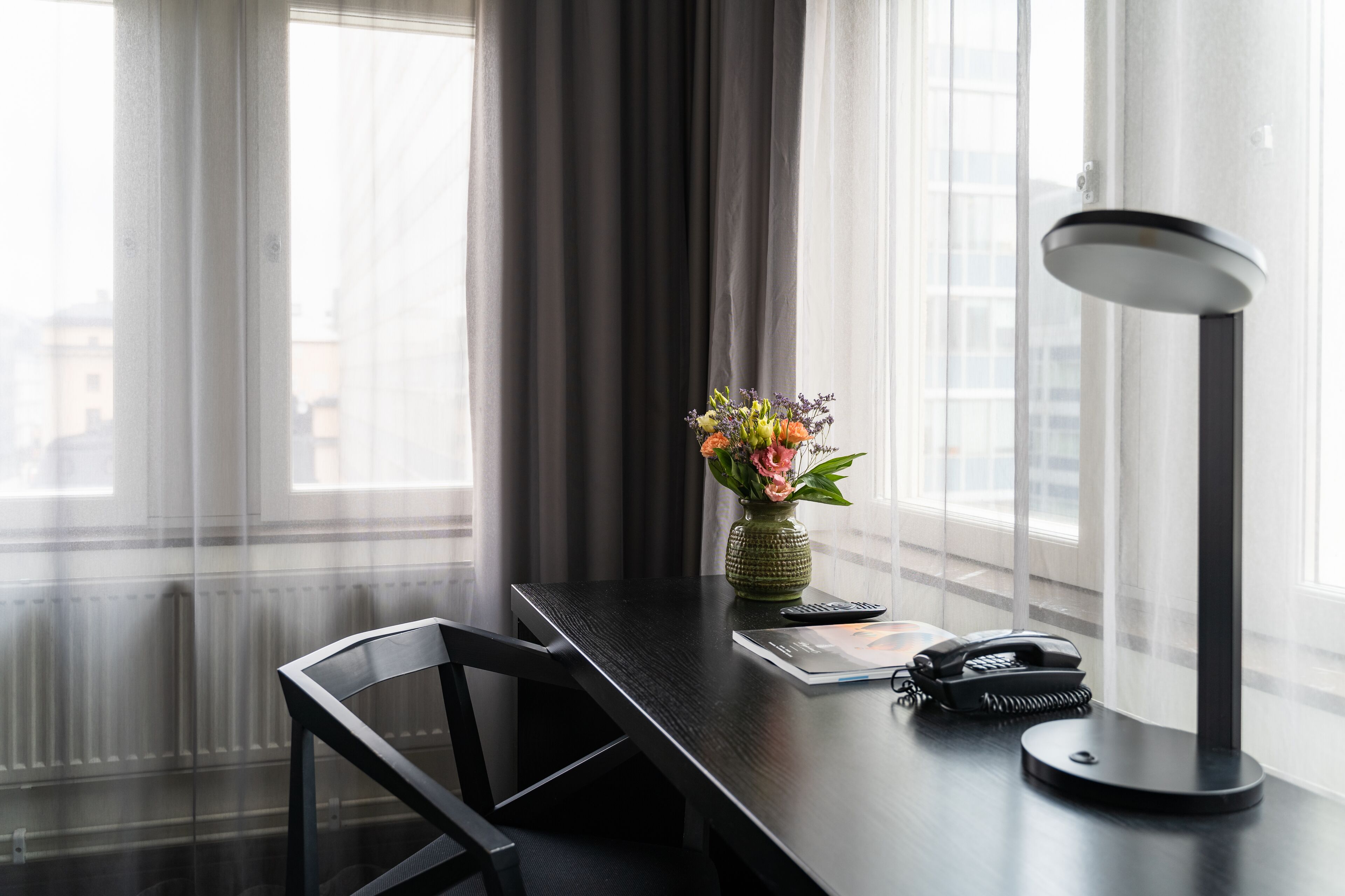 A modern office chair, a desk with a vase of flowers, a lamp, and a telephone.