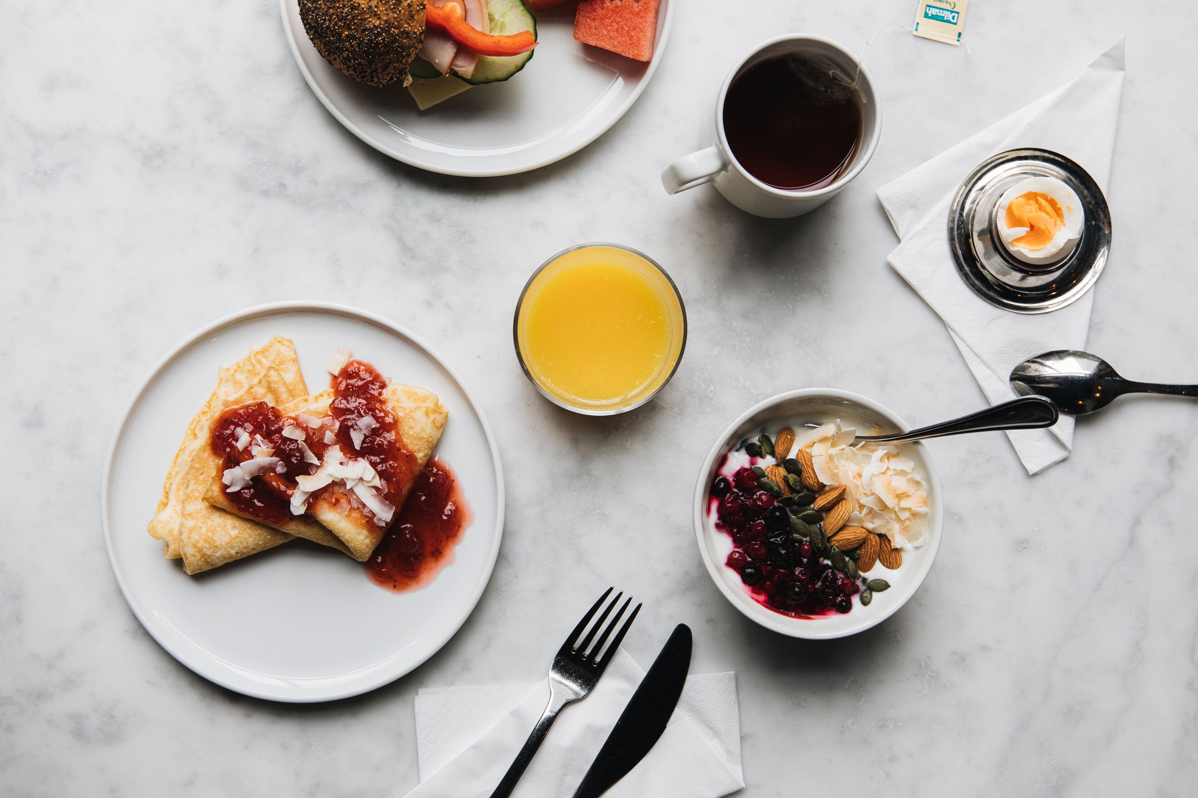 A breakfast setting with a plate of pancakes, a glass of orange juice, a bowl of yogurt with berries, a cup of coffee, and a plate with a fruit salad.