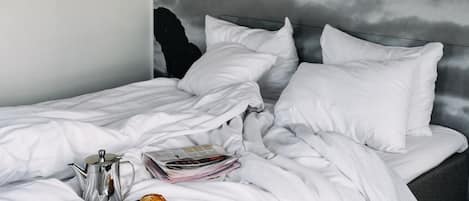 Una cama bien hecha con ropa blanca, un hervidor plateado, una taza y un plato con un pastel.