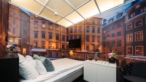 Habitación de hotel moderna con una cama, un escritorio y un televisor grande. Se aprecia una vista panorámica de la ciudad a través de las ventanas.