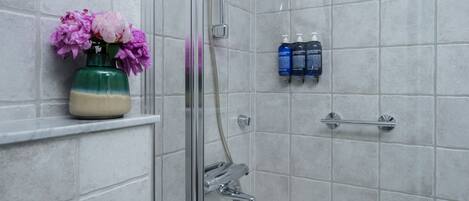 Un baño con ducha, un florero con flores y artículos de aseo en un estante.