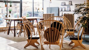 Interior moderno de café con sillas y mesas de madera, y plantas en macetas.