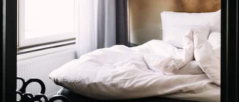 Una cama bien hecha con ropa blanca, una ventana con cortinas y una pared con un mural de temática náutica.