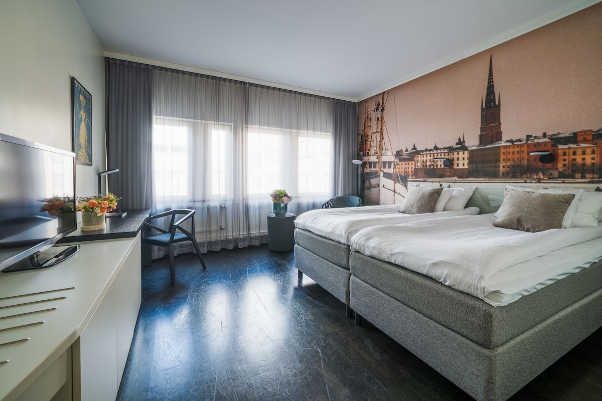Una habitación de hotel moderna con una cama grande, un escritorio y un mural con vistas a la ciudad.