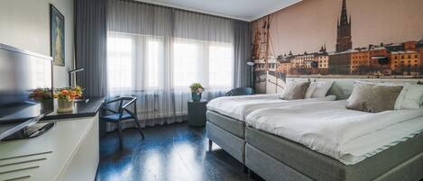 A modern hotel room with a large bed, a desk, and a cityscape mural on the wall.